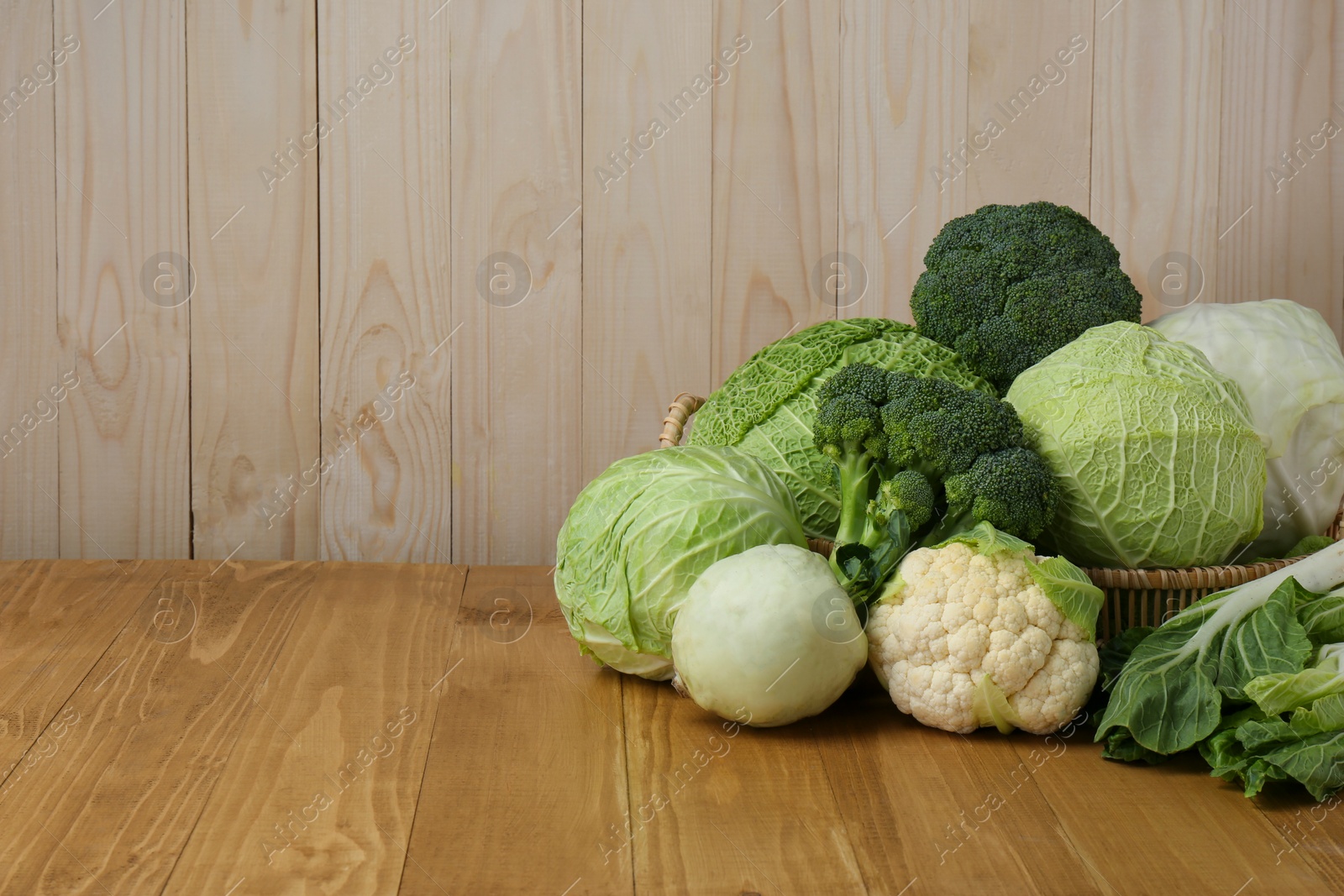 Photo of Many different types of fresh cabbage on wooden table. Space for text