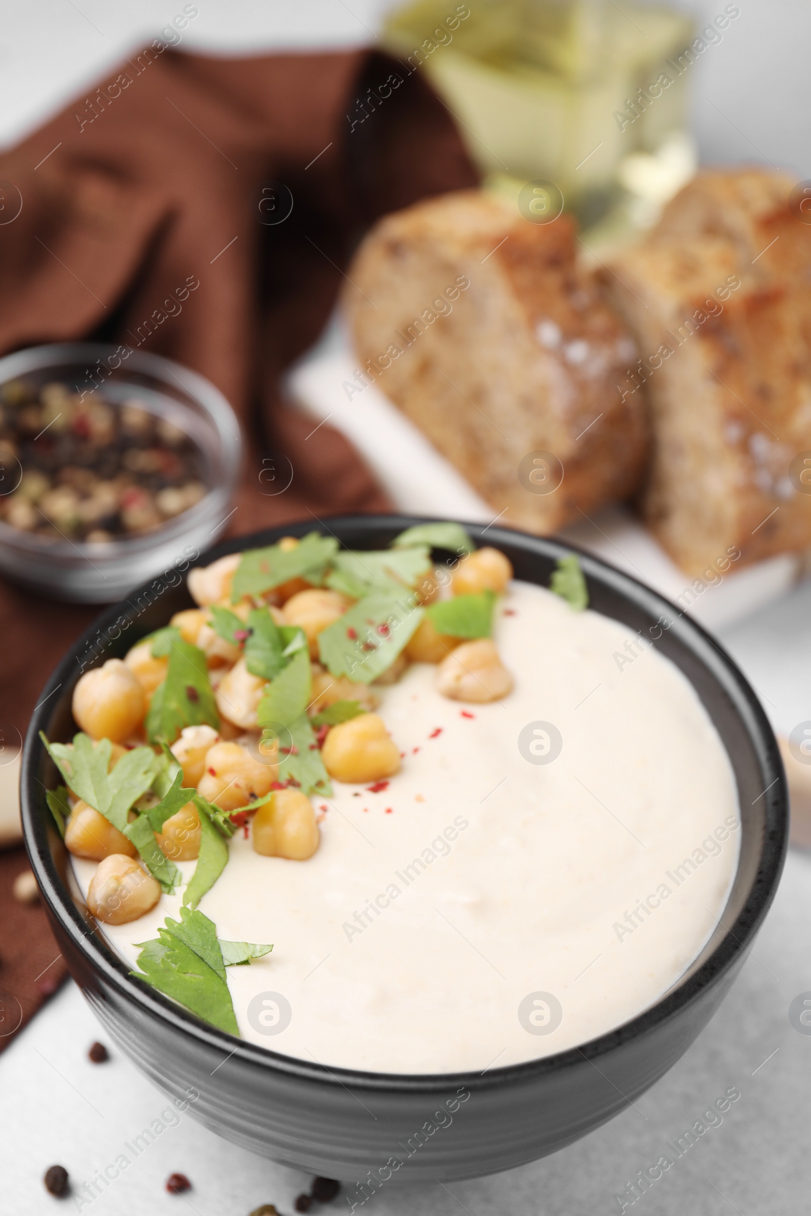 Photo of Tasty chickpea soup in bowl, bread and spices served on light grey table