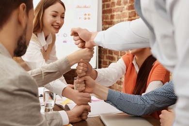 Photo of Office employees joining hands during meeting at work