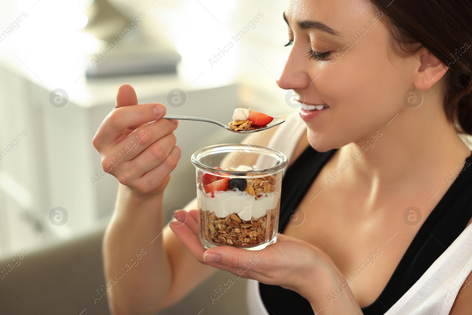 Photo of Woman eating tasty granola with fresh berries and yogurt at home, closeup