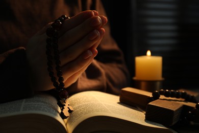 Woman praying at table with burning candle and Bible, closeup