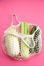 Photo of String bag with different vegetables on bright pink background, top view