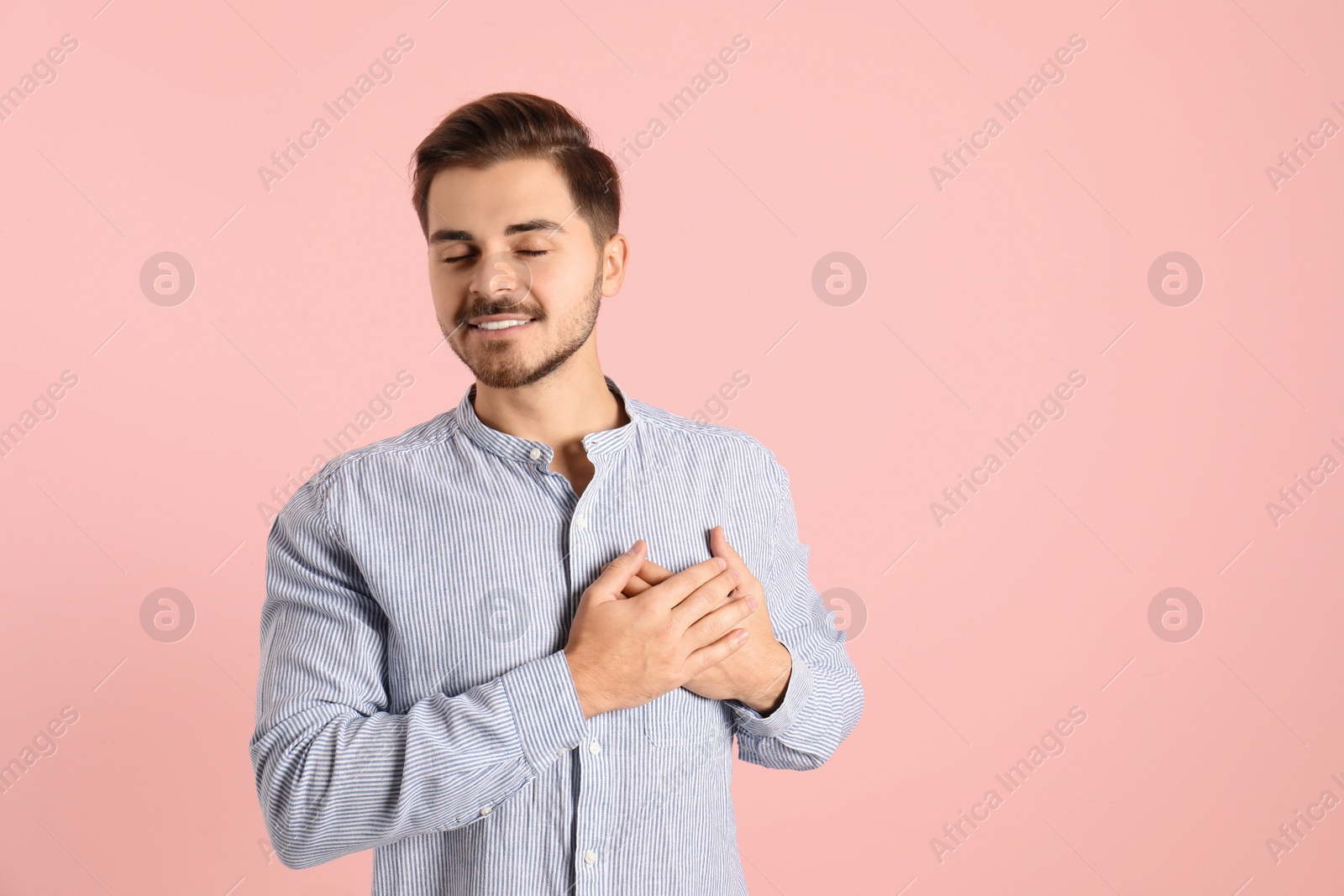 Photo of Portrait of young man holding hands near heart on color background. Space for text