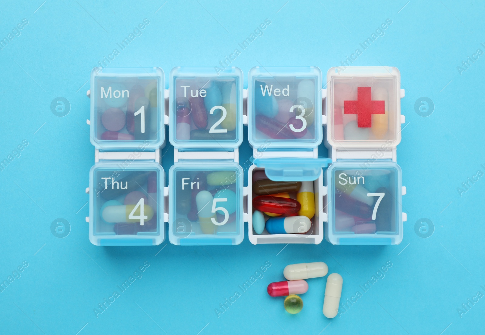 Photo of Pill box with medicaments on light blue background, flat lay