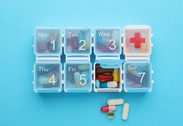 Photo of Pill box with medicaments on light blue background, flat lay