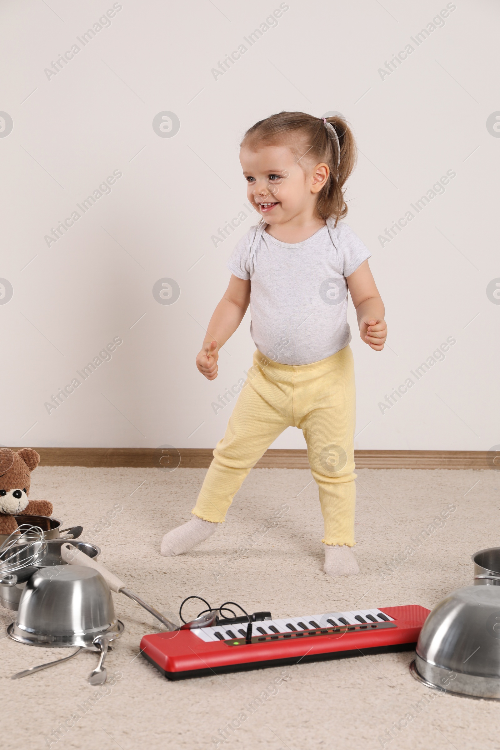 Photo of Cute little girl with cookware and toy piano at home