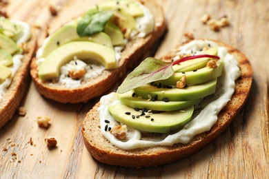 Photo of Delicious bruschettas with avocado served on wooden board, closeup