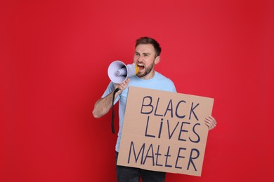 Emotional man shouting into megaphone while holding sign with phrase Black Lives Matter on red background. End Racism