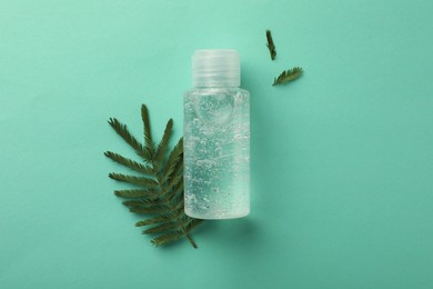 Photo of Bottle of cosmetic gel and leaves on turquoise   background, flat lay