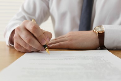 Notary signing document at wooden table, closeup