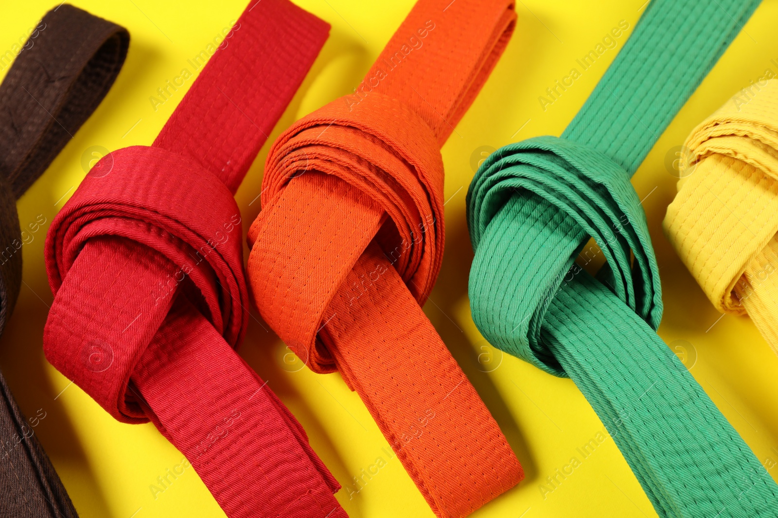 Photo of Colorful karate belts on yellow background, flat lay