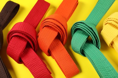 Colorful karate belts on yellow background, flat lay