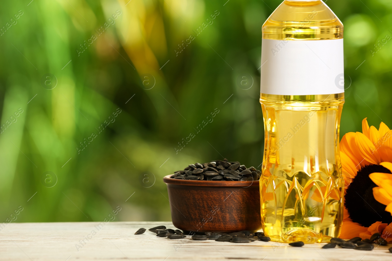 Photo of Sunflower cooking oil, seeds and yellow flowers on white wooden table outdoors. Space for text