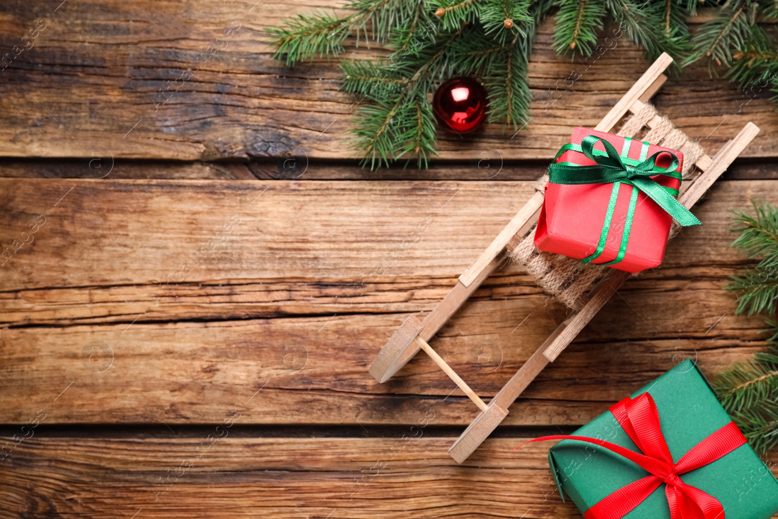 Photo of Flat lay composition with sleigh, fir tree branches and gift boxes on wooden table, space for text