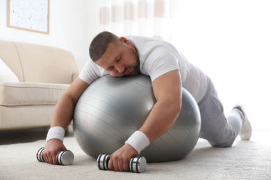 Photo of Lazy overweight man with sport equipment sleeping on floor at home