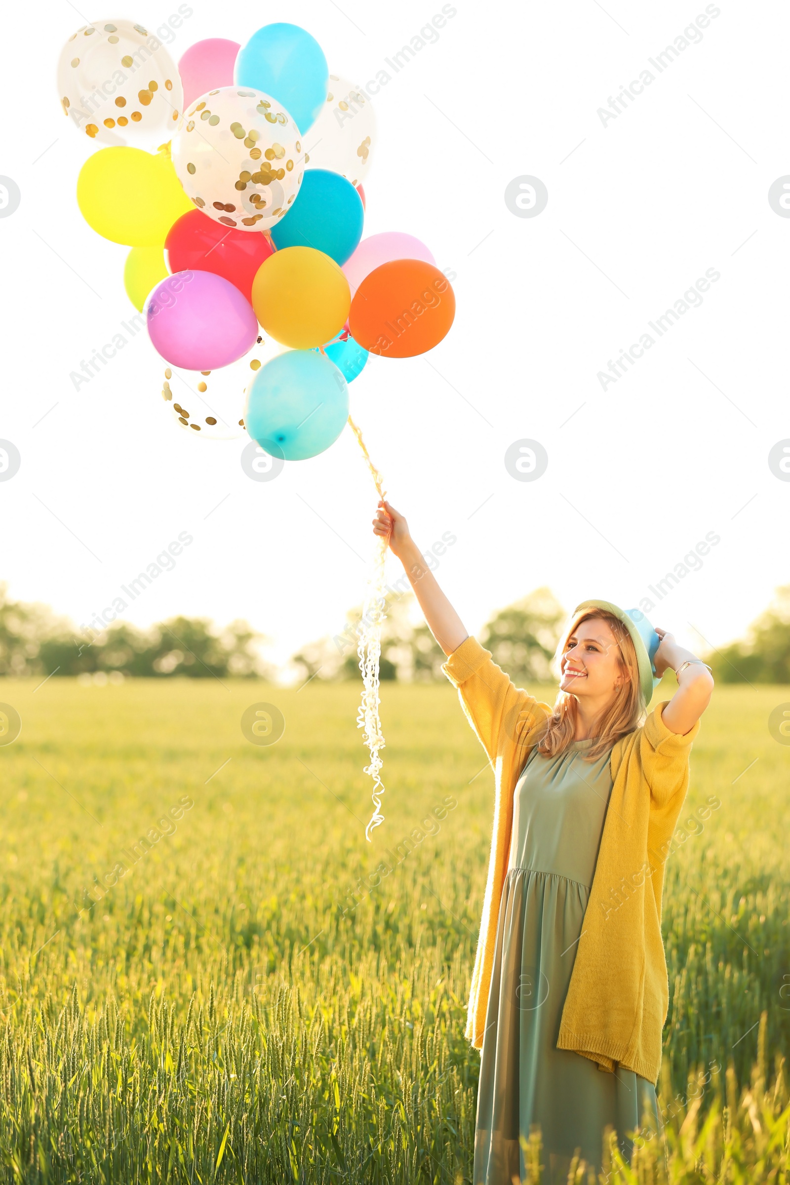 Photo of Young woman with colorful balloons in field on sunny day