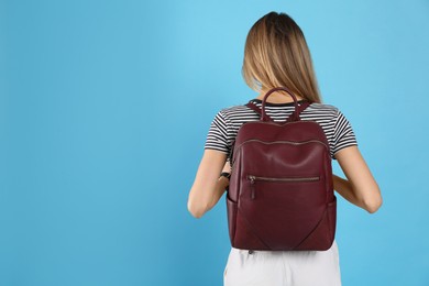 Photo of Woman with backpack on light blue background, back view. Space for text