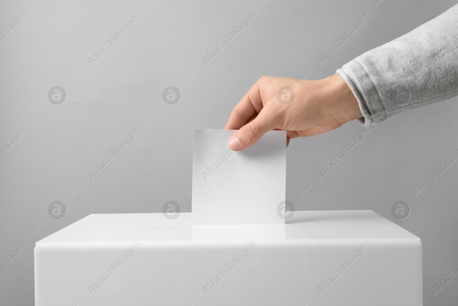 Photo of Man putting his vote into ballot box on light background, closeup