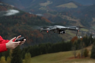 Photo of Woman operating modern drone with remote control in mountains, closeup
