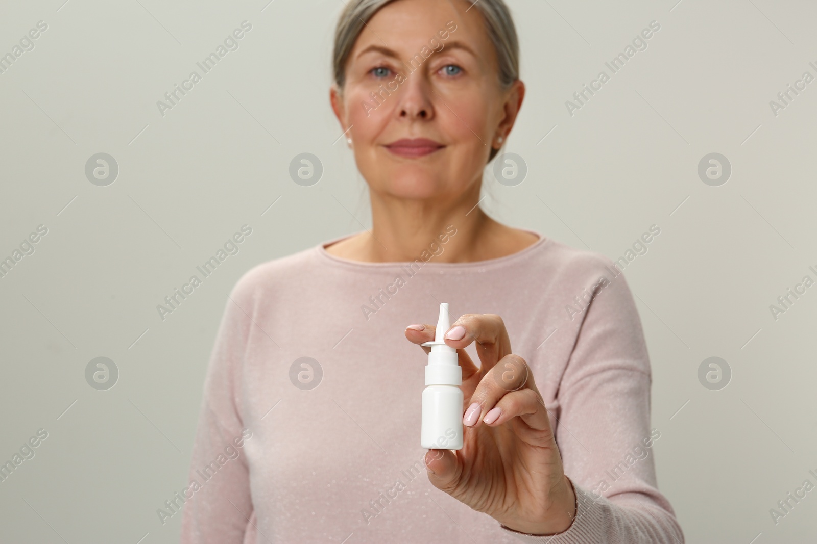 Photo of Woman holding nasal spray on light grey background, focus on bottle