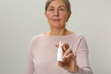 Photo of Woman holding nasal spray on light grey background, focus on bottle