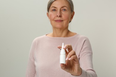 Woman holding nasal spray on light grey background, focus on bottle