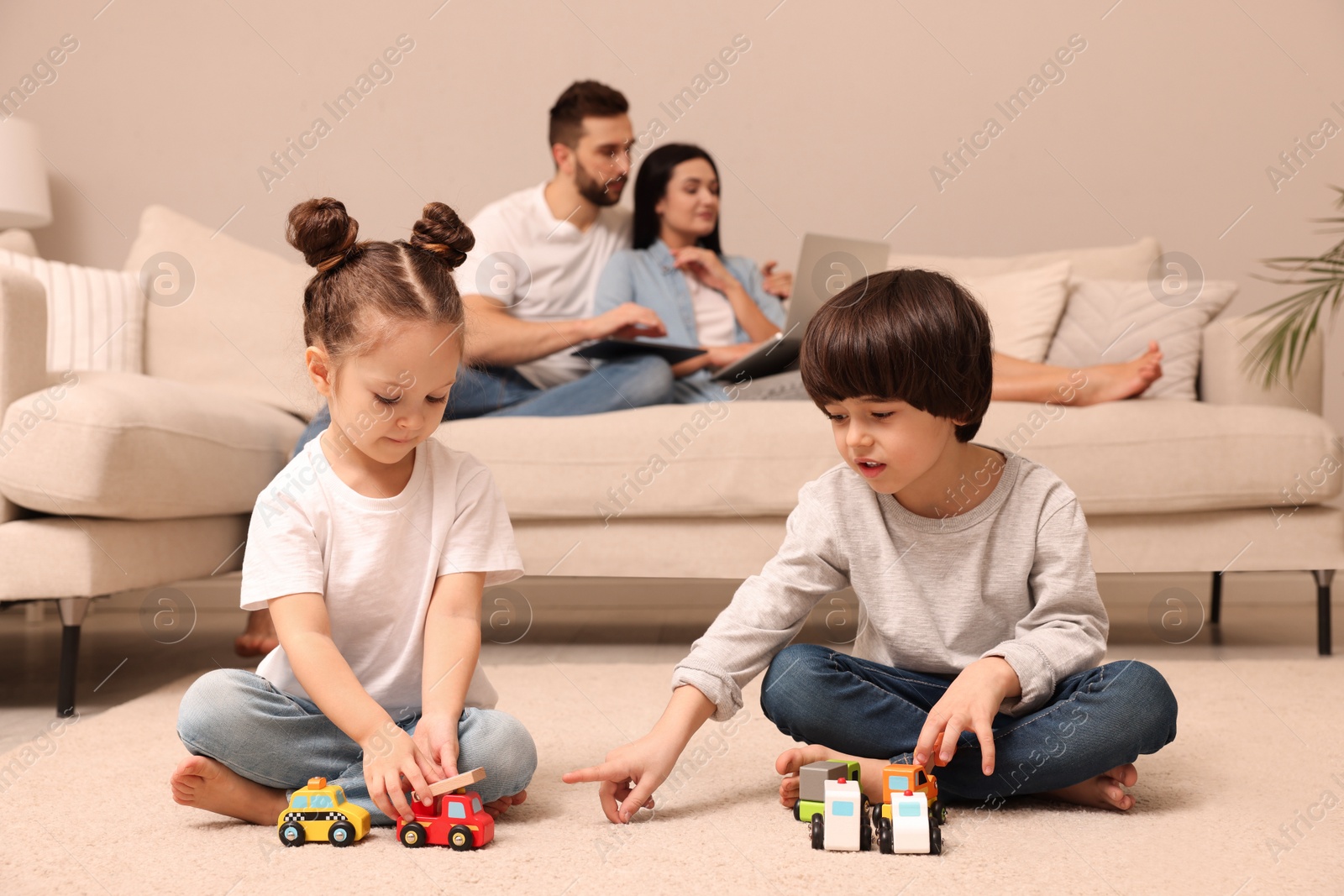 Photo of Cute children playing with toys while parents using gadgets on sofa in living room