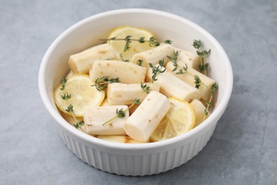 Photo of Dish with raw salsify roots, lemon and thyme on light grey table, closeup