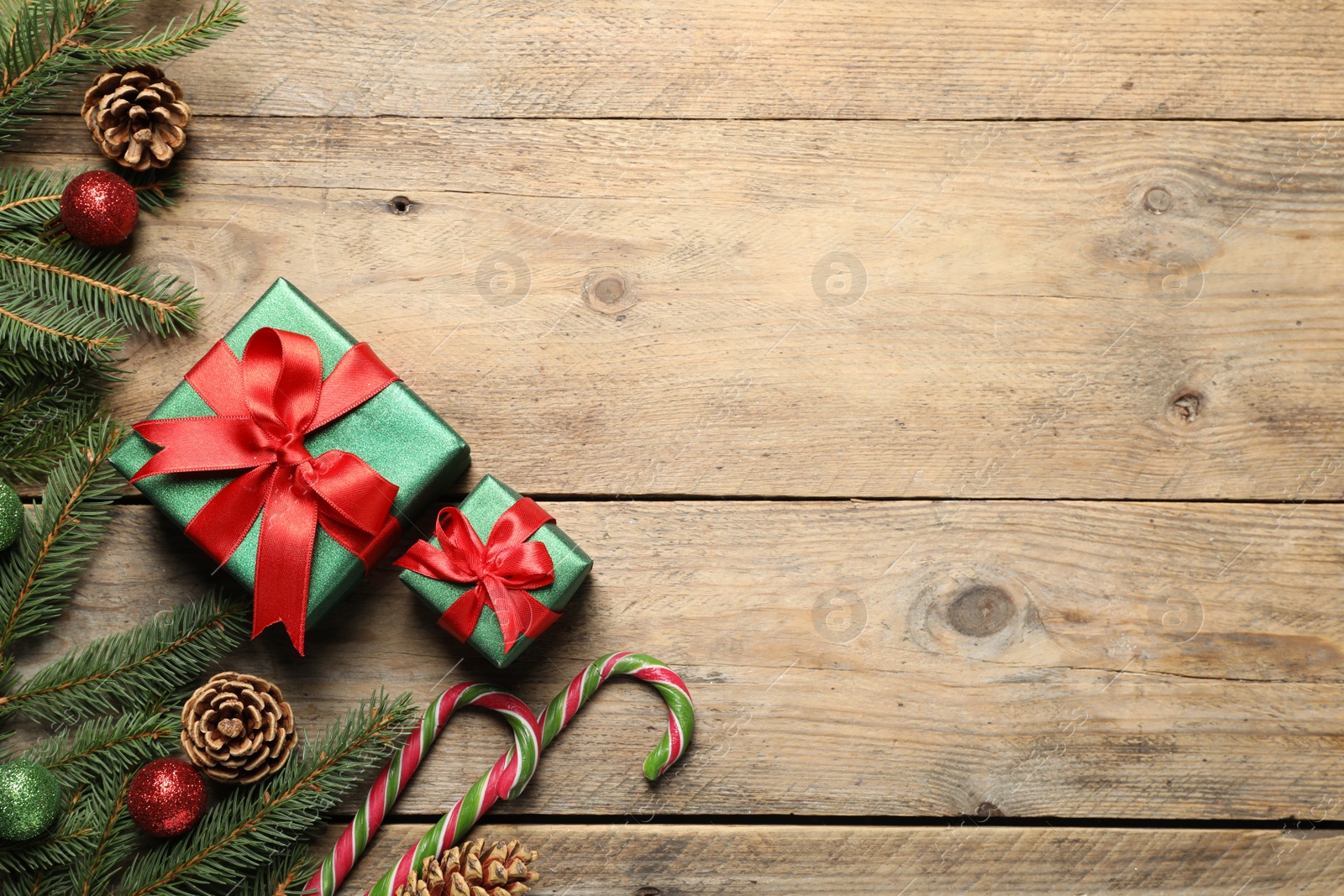 Photo of Gift boxes, candy canes, fir tree branches and Christmas decor on wooden table, flat lay. Space for text