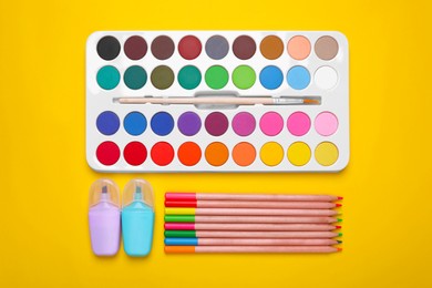 Photo of Watercolor palette, colorful pencils and markers on yellow background, flat lay