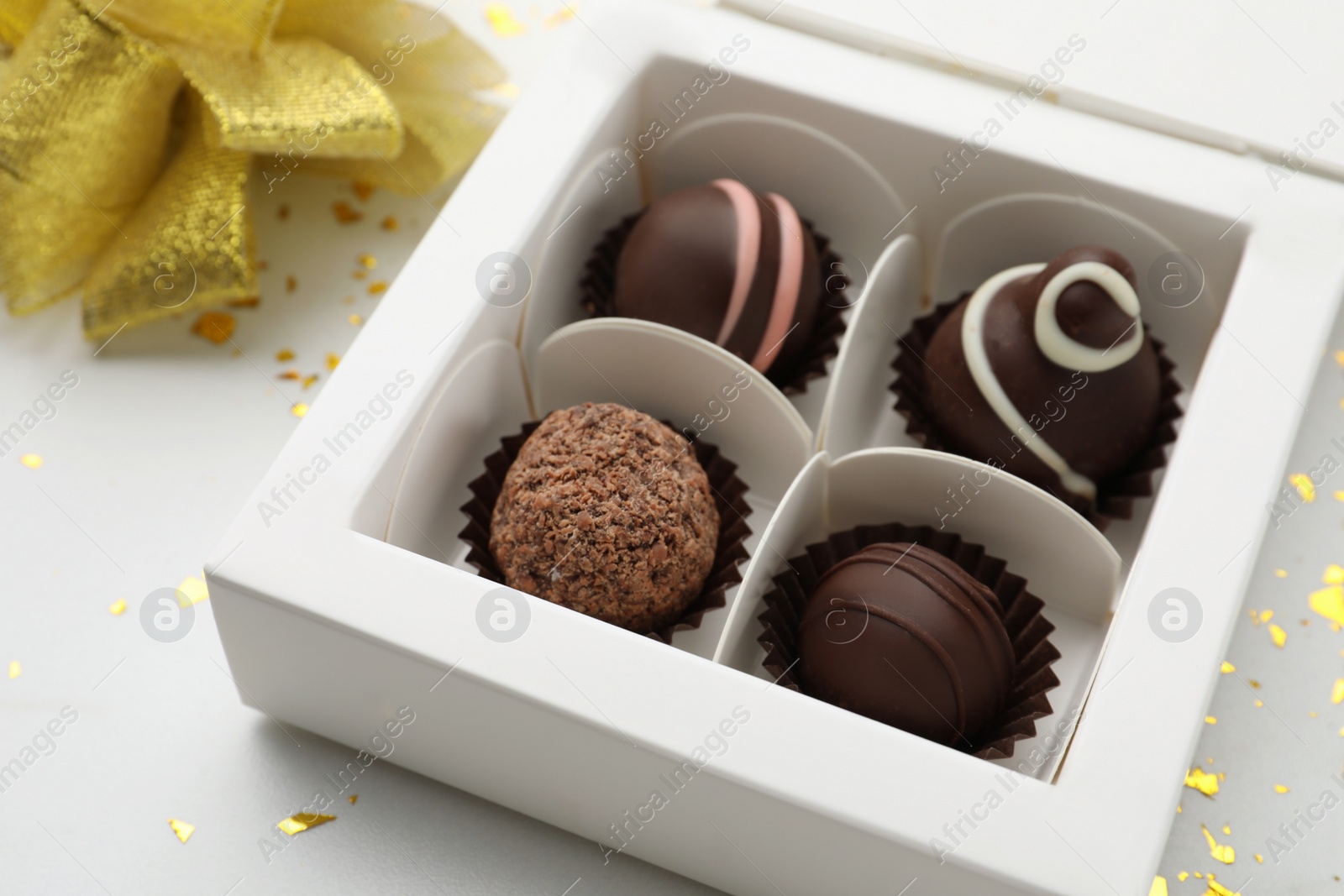 Photo of Different delicious chocolate truffles in box, bow and confetti on white background, closeup