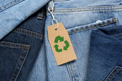 Different jeans with recycling label as background, top view