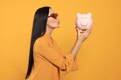 Young woman with piggy bank on orange background