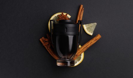 Photo of Bottle of perfume, cloves, lemon slices and cinnamon sticks on black background, top view