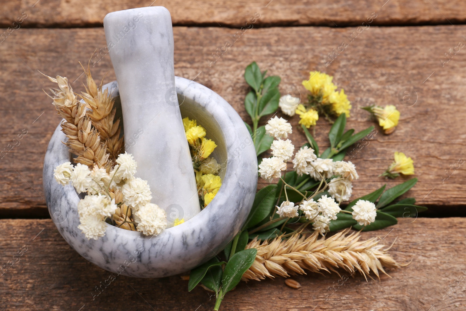 Photo of Mortar with pestle, dry flowers and ears of wheat on wooden table