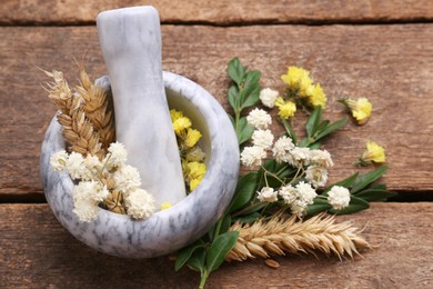 Mortar with pestle, dry flowers and ears of wheat on wooden table