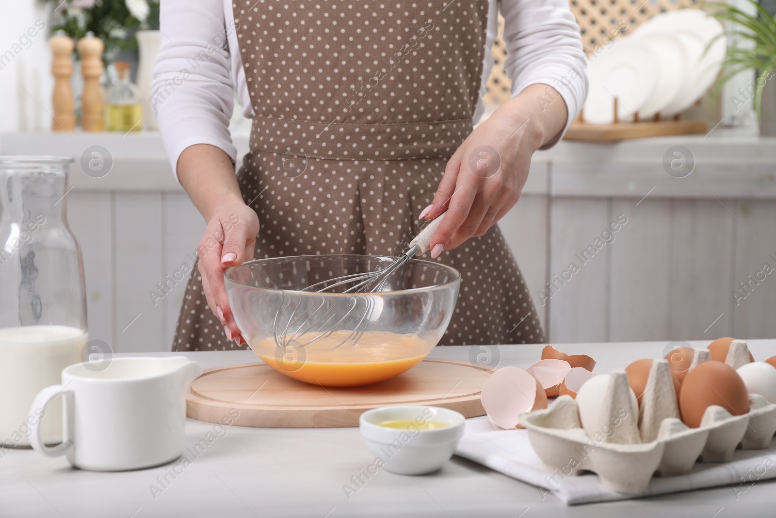 Photo of Woman whisking eggs in bowl at table indoors, closeup