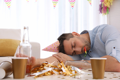 Photo of Young man with festive cap sleeping at table after party