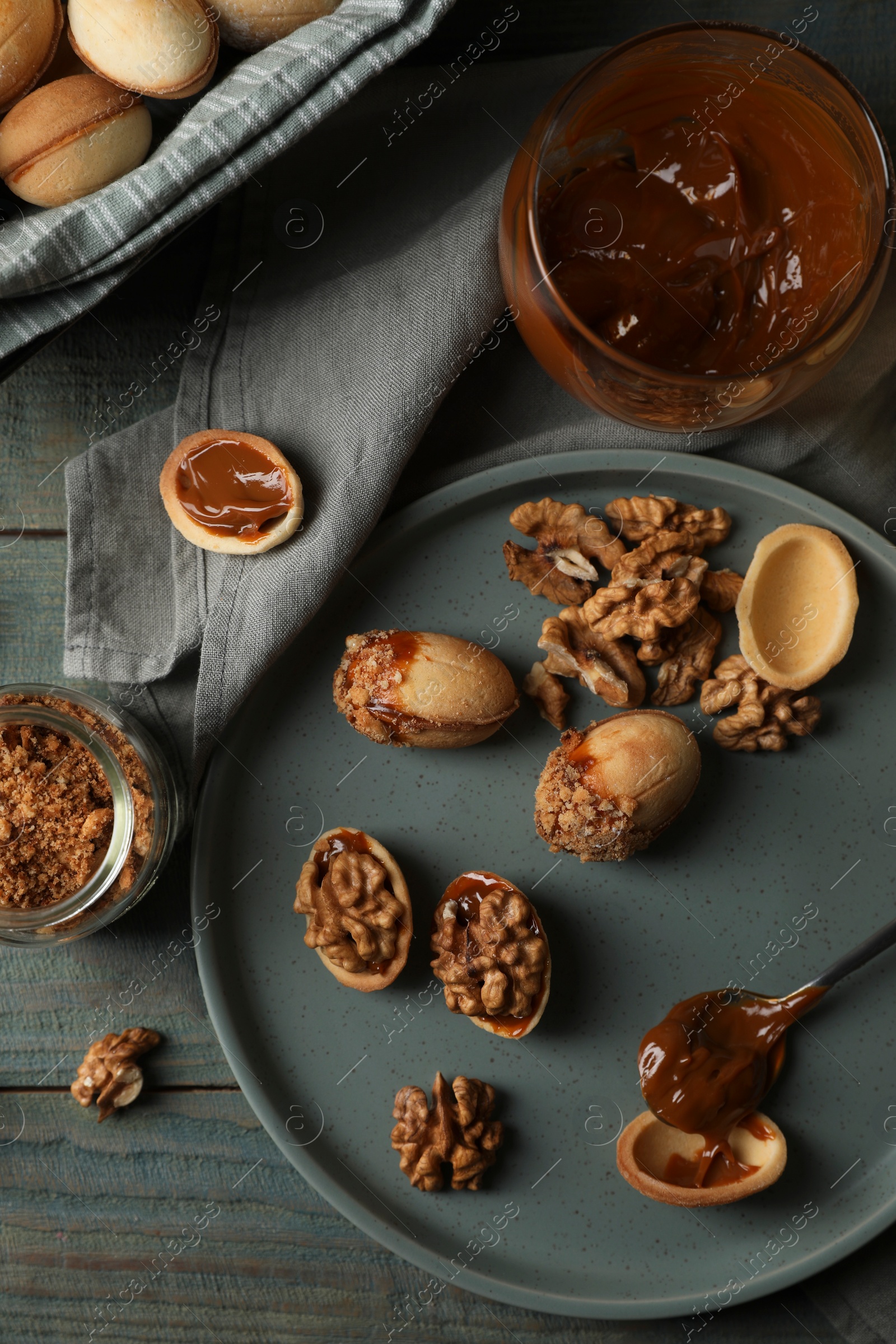 Photo of Freshly baked homemade walnut shaped cookies with nuts and boiled condensed milk on wooden table, flat lay