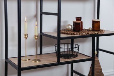 Photo of Stylish shelving unit with burning candles and decor near white wall indoors. Interior design