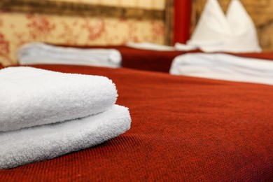 Clean folded towels on bed in hotel room, closeup. Space for text