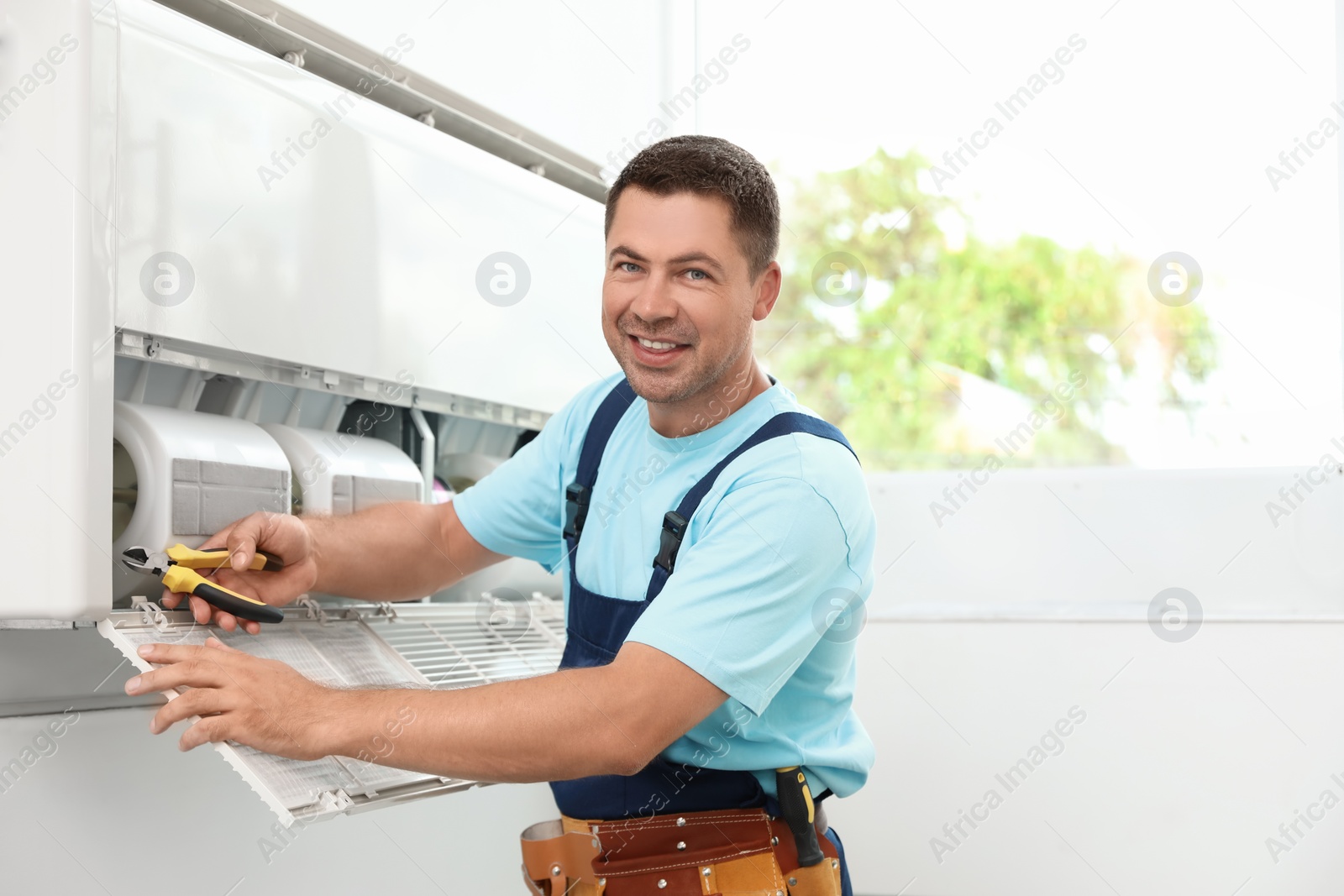 Photo of Male technician repairing modern air conditioner indoors