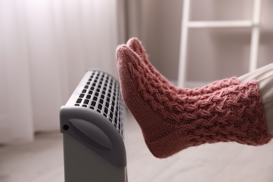 Photo of Woman warming feet on electric heater at home, closeup