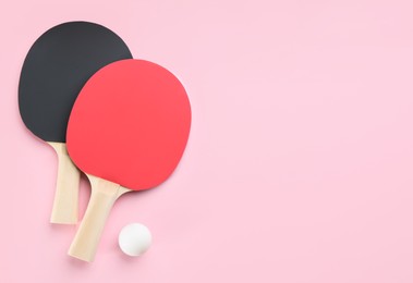 Photo of Ping pong rackets and ball on pink background, flat lay. Space for text