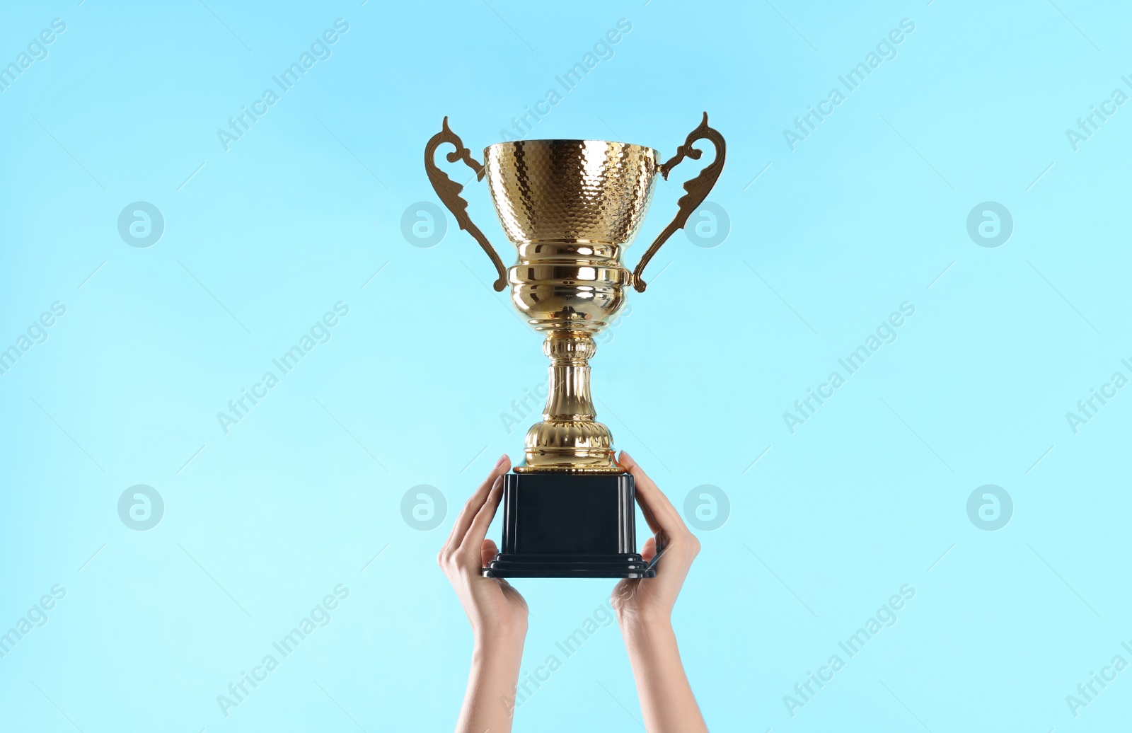 Photo of Woman holding gold trophy cup on light blue background, closeup