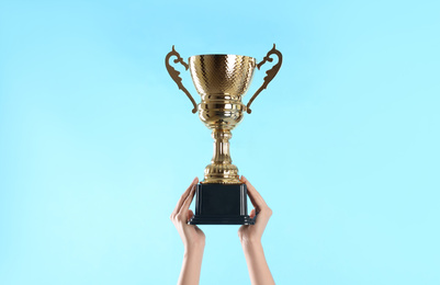 Photo of Woman holding gold trophy cup on light blue background, closeup