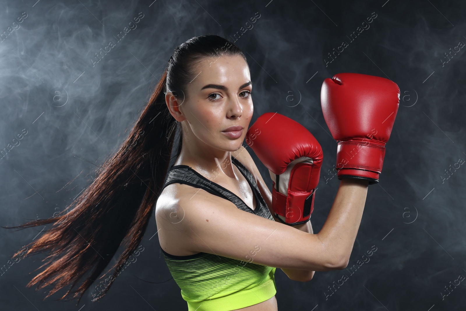 Photo of Beautiful woman wearing boxing gloves training in smoke on black background