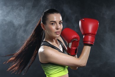 Beautiful woman wearing boxing gloves training in smoke on black background