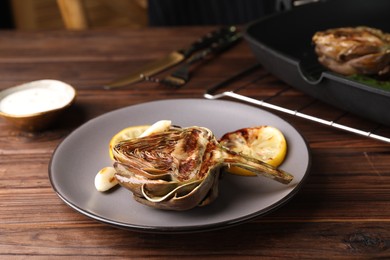 Tasty grilled artichoke served on wooden table, closeup