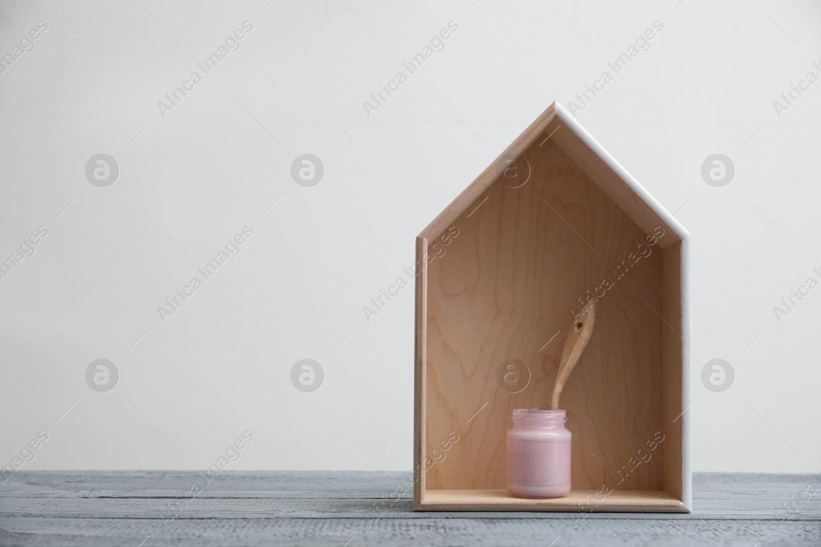 Photo of Brush with paint and wooden house model on grey table. Space for text